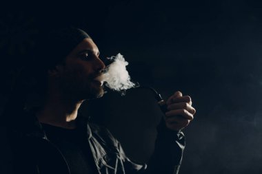 Siyah arka planda pipo içen bir adam. Profil portresi.