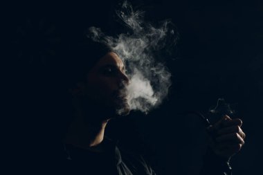 Siyah arka planda pipo içen bir adam. Profil portresi.