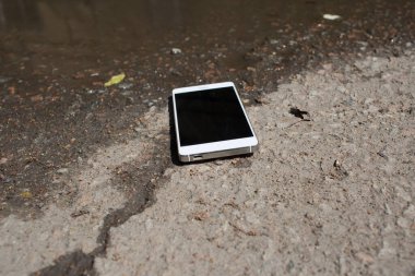 Mobile phone lying on pavement in puddle clipart