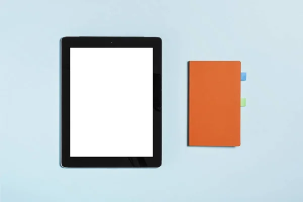 Tablet-Computer mit orangefarbenem Cover-Notizbuch auf blauem Hintergrund. — Stockfoto