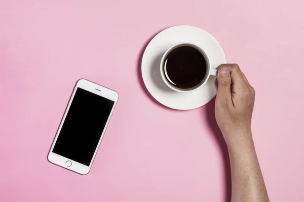 Segurando telefone e xícara de café no fundo rosa . — Fotografia de Stock