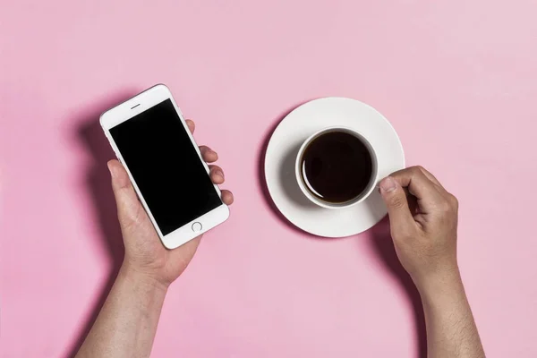 Segurando telefone e xícara de café no fundo rosa . — Fotografia de Stock