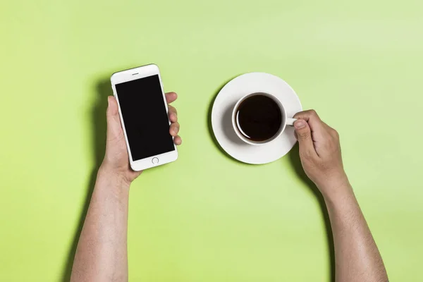Segurando xícara de café com telefone no fundo verde . — Fotografia de Stock