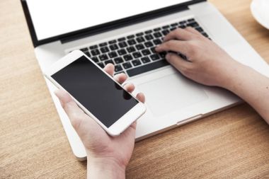 telefonu ve laptop yaz ahşap masanın üzerinde tutan adam.