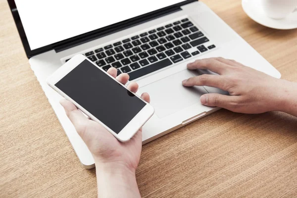 telefonu ve laptop yaz ahşap masanın üzerinde tutan adam.