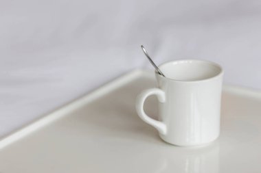 Seramik bardak, çay kaşığı ve beyaz çarşaf üzerinde beyaz tepsi.
