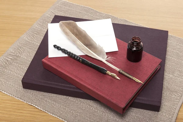 feather/fountain pen, ink and book on wooden desk.