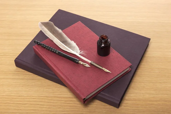 feather/fountain pen, ink and book on wooden desk.