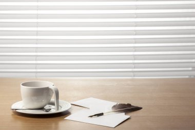 Bir kahve fincanı, tüy tüy kalem, mektup, zarf üzerinde beyaz kör arkasında office desk(table).