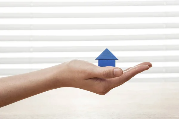 A female(woman) hand hold a house(made in wood blocks) white blind background and table.