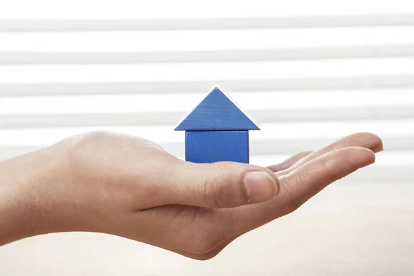 A female(woman) hand hold a house(made in wood blocks) white blind background and table.