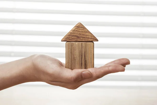 A female(woman) hand hold a house(made in wood blocks) white blind background and table.