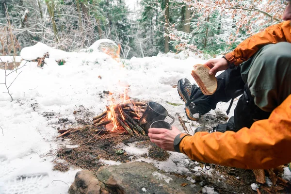 Hombre no reconocido prepara té en un fuego en el bosque, sosteniendo un sándwich —  Fotos de Stock