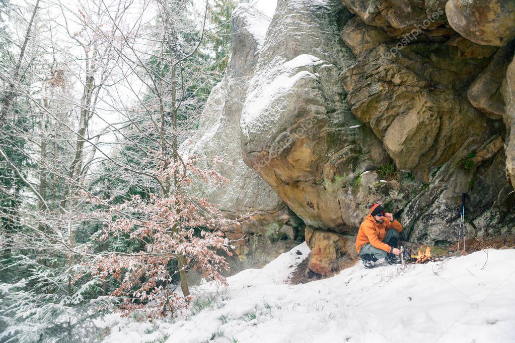 hiker prepares food on fire, while snowfall in the woods, surviving