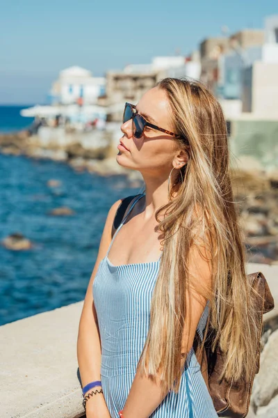 Jonge mooie vrouw met lang blond haar in zonnebril poseren door de blauwe zee Rechtenvrije Stockfoto's