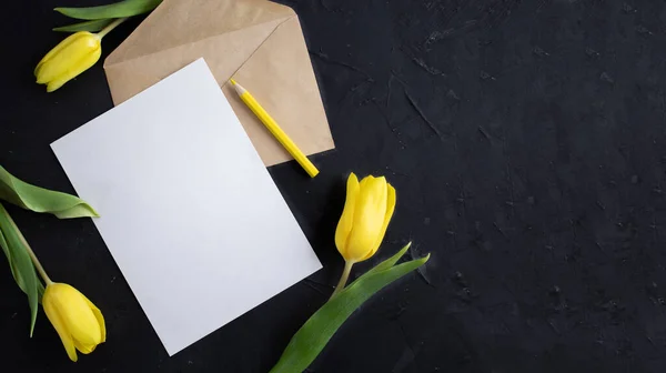 Gula tulpaner på kanten av vitt papper för text på en mörk bakgrund. Ett blankt papper med ett kuvert. Kopiera utrymme — Stockfoto
