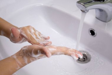 Musluğun altında ellerini yıkamak ya da musluğu sabunla yıkamak. Çocuk musluğun altında sabun ve ellerini yıkıyor. Hijyen konsepti el detayı.