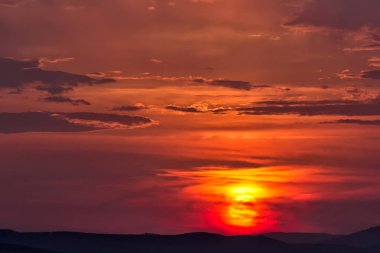 Tepeler üzerinde büyük bir güneş ile bulutlu renkli gün batımı, Enisala, Dobrogea, Romanya