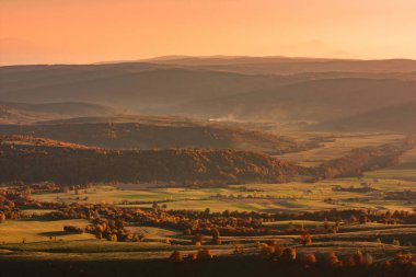 Beautiful aerial view of an autumn landscape of a green valley with colored trees in the golden hour light of the sunset, Sfanta Ana, Harghita, Romania