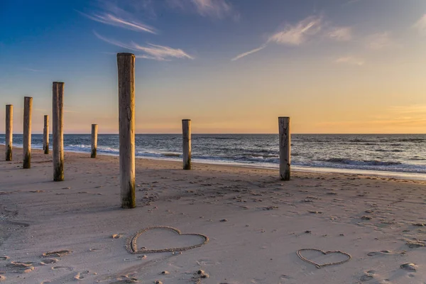 Kumsalda altın saatin ışığı Kumda ahşap kazıklar ve kalplerle Petten, Hollanda, Hollanda, Hollanda, Kuzey Denizi