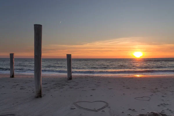 Krásný Západ Slunce Pláži Dřevěnými Pilíři Kresbami Srdcí Písku Petten — Stock fotografie