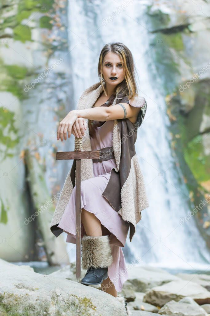 Beautiful blonde viking woman with a shield and a sword near a waterfall, Pruncea Casoca, Romania