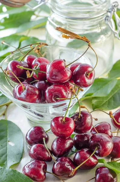 Ripe maroon cherries in a glass vase and a jar — Stock Photo, Image