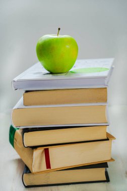 Bir yığın kitap ve beyaz arka planda yeşil elma.