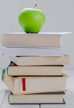 Bir yığın kitap ve beyaz arka planda yeşil elma.