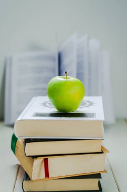 Bir yığın kitap ve beyaz arka planda yeşil elma.