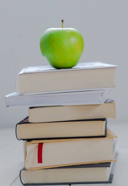 Bir yığın kitap ve beyaz arka planda yeşil elma.