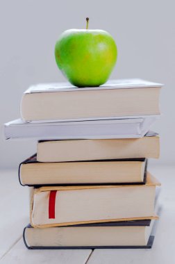 Bir yığın kitap ve beyaz arka planda yeşil elma.