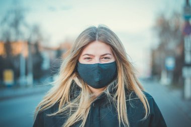 Tıbbi maskeli bir kızın yakın plan portresi. Salgın Koronavirüs Karantinası. Covid 19. Koruyucu maskeli bir öğrenci. Siyah koruyucu maskeli ve siyah elbiseli genç bir kız. Görüş.