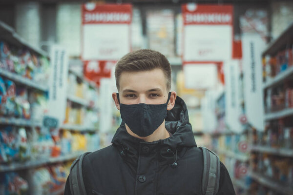Closeup portrait of a young guy in a medical mask. Pandemic. Coronavirus. Quarantine. Covid19. Student in a protective mask. Gloomy young man in a black mask and black clothes on a dark background.
