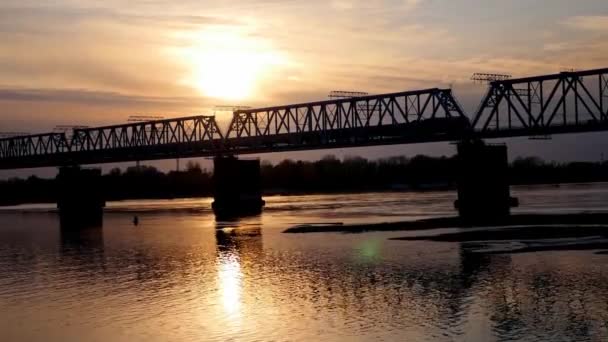 Поїзд через річку на заході сонця — стокове відео