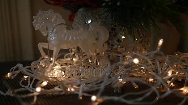 Plastic speelgoed paard op de kerstboom in slingers rond fir takken in een vaas, — Stockvideo