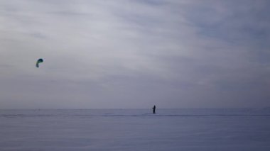 genç bir adam bir paraşüt kışın, 4 k donmuş bir göl kenarında dururken kiteboarding üzerinden denetlemek öğrenir