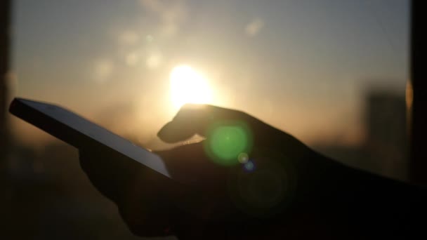 Sostener el teléfono en su mano sobre un fondo de puesta de sol, con deslumbramiento del sol, 4k — Vídeos de Stock