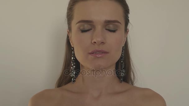 Ursnygg flicka som står på en vit bakgrund i en örhängen, höjer huvudet och ser mystisk blick in i kameran, 1920 x 1080 — Stockvideo