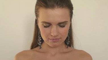 Harika kız poz güzel uzun küpe model ve yavaş yavaş kafası esrarengiz bakışlarını kaşları altından yükseltir. Ağır çekim.