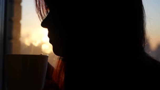 Vacker flicka dricker kaffe vid solnedgången i staden mot fönstret, 3840 x 2160, 4k — Stockvideo