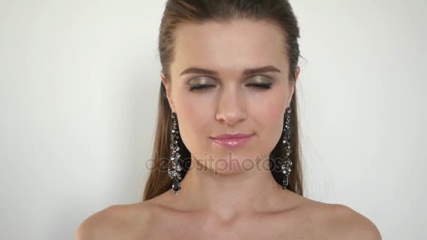 A beautiful young girl with embellishments in his ears, stands on a white background in the studio posing for the camera, raises his head and looks mysterious look directly into the camera, 4k — Stock Video