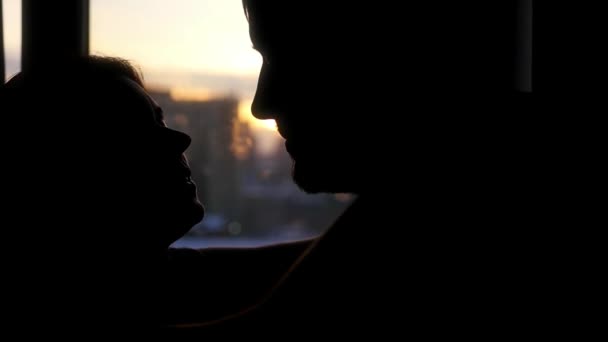 Joven pareja romántica hermosa mirándose los ojos, de pie contra el telón de fondo de una hermosa puesta de sol en la ciudad y un suave beso en los labios y la barbilla. Movimiento lento — Vídeo de stock