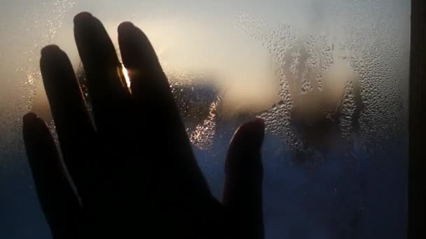 Die weibliche Hand im Vordergrund wischt die Wassertropfen aus dem Glas vor dem Hintergrund eines wunderschönen Sonnenuntergangs und des Himmels ab und versucht, die Sonne zu berühren. 1920x1080 — Stockvideo