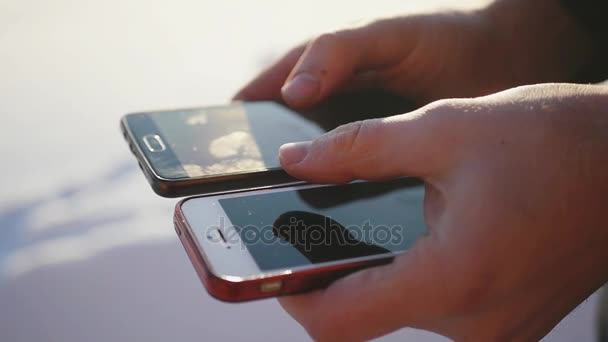 A business man, holding two mobile phones in his hands, thumbs his fingers on the monitor. 1920x1080 — Stock Video