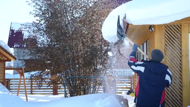 Die großen weißen Schneewehen auf dem Dach des Hauses werden von einem Mann mit einer Plastikschaufel weggeworfen. hd, 1920x1080. Zeitlupe. — Stockvideo