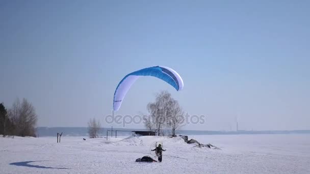 Een man op een paraglider landt op de sneeuw op een blauwe parachute. 4 k. 3840 x 2160 — Stockvideo