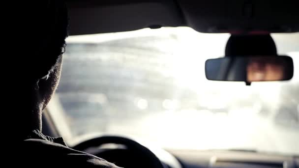 El hombre cabalga en el coche a través de la ciudad en el fondo del sol brillante de primavera, proteger sus ojos de ella. En cámara lenta. 1920x1080 — Vídeo de stock