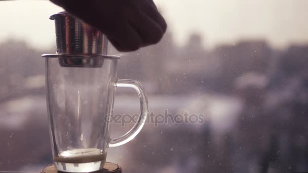 Haciendo café fresco en Asia, una gota de café cae en una taza transparente sobre el fondo de un paisaje borroso de la ciudad. 4k, 3840x2160 — Vídeo de stock