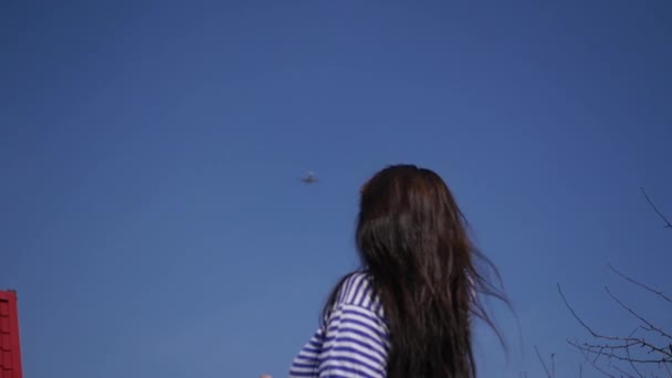 Young girl is watching the flying airplane against the blue sky. Slow motion. 1920x1080. HD — Stock Video